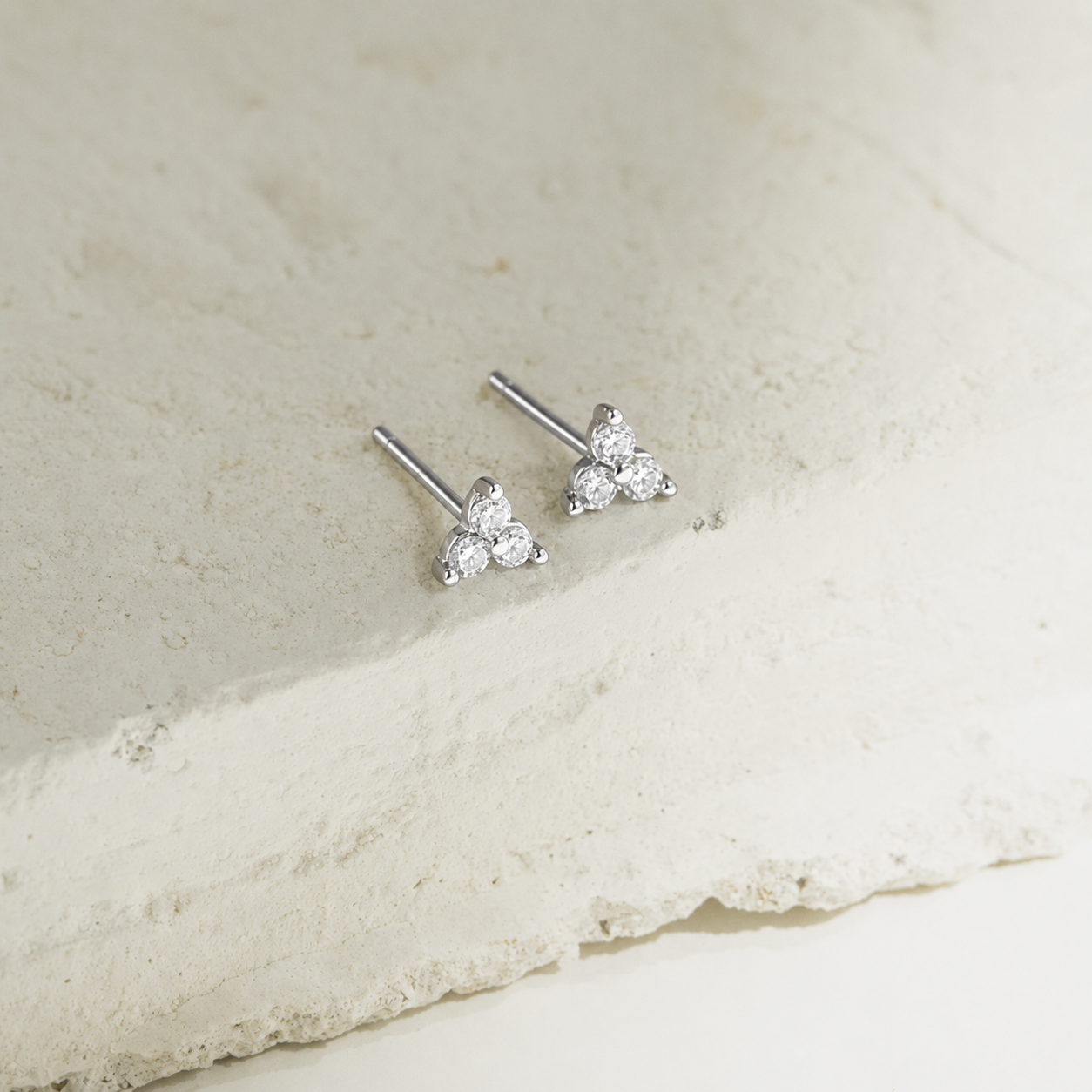 Silver triangle-shaped stud earrings on a light stone surface